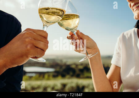 Close up of hands of a couple toasting glasses of white wine sitting outdoors. Cropped shot of a couple toasting wine. Stock Photo