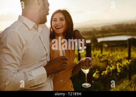 Smiling couple holding wine glasses standing together on a sunny day in a wine farm. Couple on a date enjoying a glass of wine and spending time toget Stock Photo