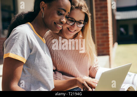 Two young people finding information for their study on laptop at college campus. Young students sitting at university campus working on laptop comput Stock Photo