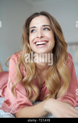 Laughing young woman in dressing gown lying in bed Stock Photo