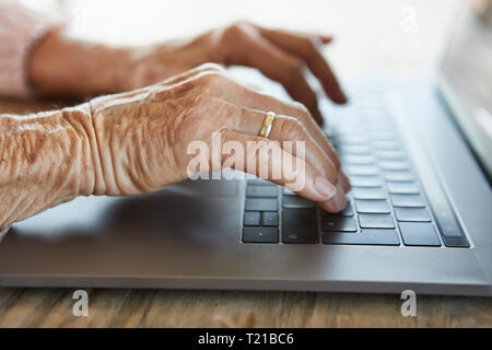 Hand of senior woman typing on keyboard of laptop, close-up Stock Photo