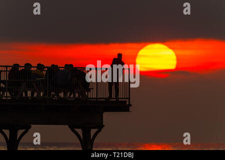 Aberystwyth, Wales. 29th Mar 2019. UK Weather: A man enjoying an evening drink at the end of the pier in Aberystwyth, on the Cardigan Bay coast of west Wales is  silhouetted by the flaming setting sun . High pressure continues to dominate the weather for much England and Wales, with settled conditions forecast to last at least another day , before more cooler conditions return. Photo:Keith Morris/Alamy Live News Stock Photo