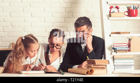 Education and knowledge day. Back to school and home schooling. Father helps children to study at home. School time of girl sisters with father Stock Photo