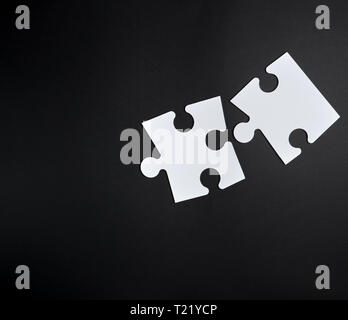 two white big puzzles on a black background, empty space. Concept in business Stock Photo