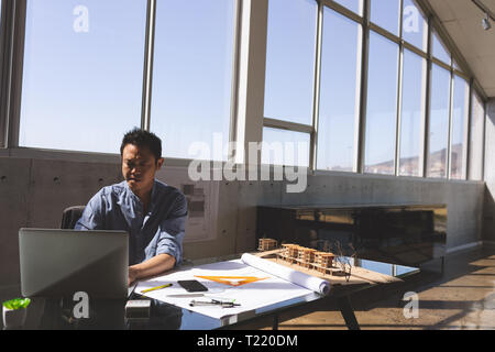 Male architect using laptop while working on blueprint at desk Stock Photo