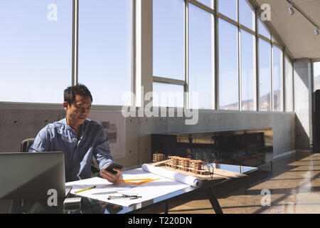 Male architect sitting at desk and using mobile phone Stock Photo