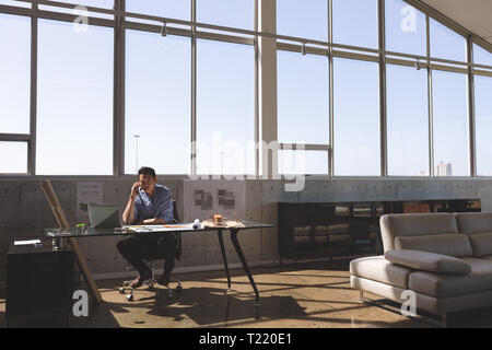 Male architect sitting at desk and talking on mobile phone Stock Photo