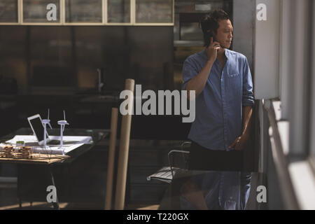 Male architect talking on mobile phone while standing near window in a modern office Stock Photo