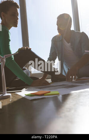Architects sitting on floor and discussing over blueprint in office Stock Photo