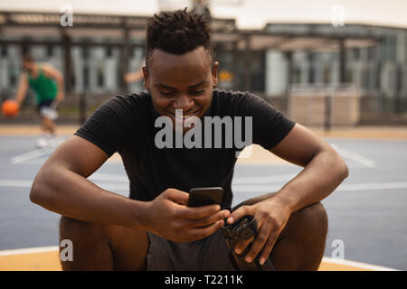 Basketball player sitting on a basketball while he is using mobile phone Stock Photo