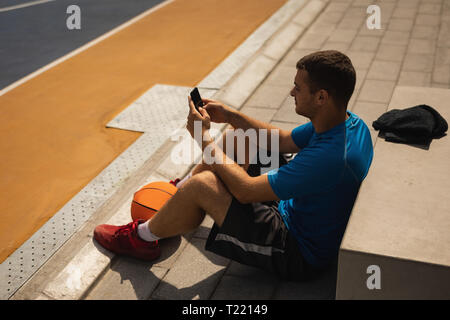 Basketball player using mobile phone while relaxing on basketball court Stock Photo