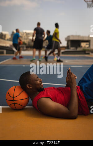 Basketball player using mobile phone while relaxing on basketball court Stock Photo