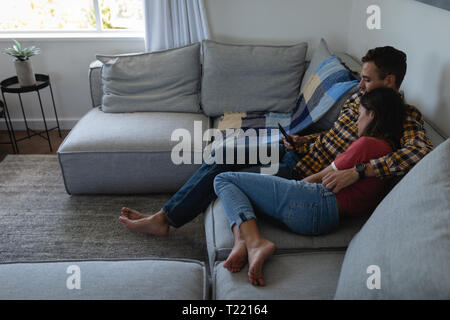 Couple using mobile phone while leaning on sofa at home Stock Photo