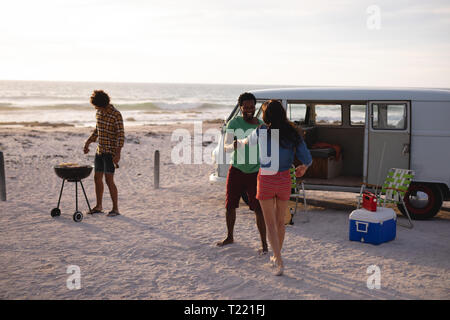 Friends dancing together on sand at beach while an other doing a barbecue Stock Photo