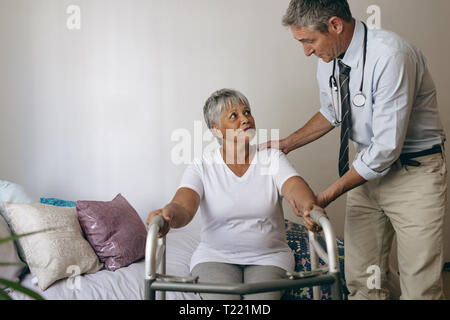 Male doctor helping senior female patient to walk with walker Stock Photo