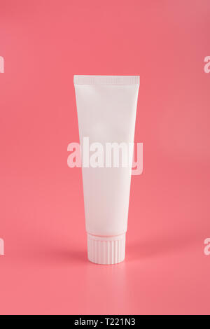 Blank white tube of toothpaste, cream or gel standing on pink background. Branding mockup Stock Photo