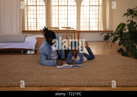 Father and son reading book while lying on floor at home Stock Photo