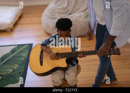 Father assisting his son to play guitar at home Stock Photo