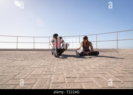 Couple doing stretching exercise on  pavement near promenade beach Stock Photo