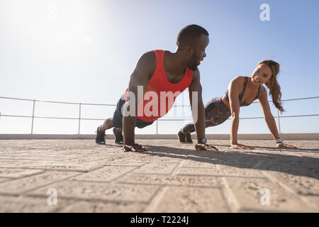 Couple interacting with each other while doing push ups on pavement Stock Photo