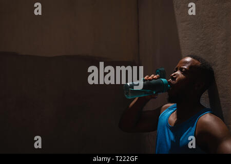 Man drinking water while standing beside the wall on a sunny day Stock Photo
