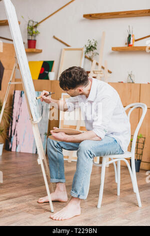 pensive artist in white shirt and blue jeans painting on canvas Stock Photo