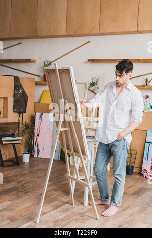 handsome artist in white shirt and blue jeans painting on canvas Stock Photo