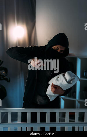 Kidnapper in black clothes aiming gun at infant child Stock Photo