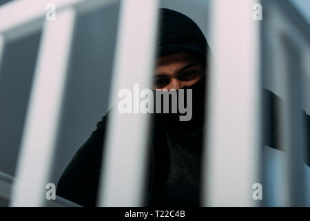 Angry criminal in black clothes and mask looking down Stock Photo