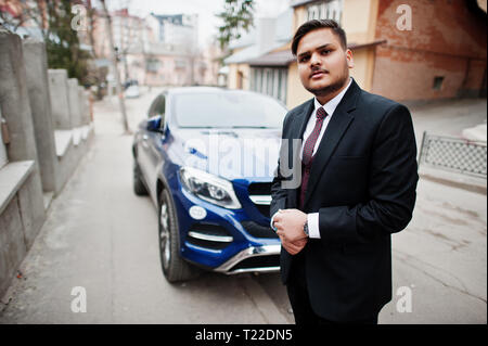 Rich indian diplomat businessman in formal wear standing against business suv car. Stock Photo
