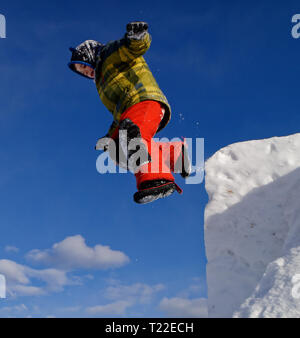 A young boy (6 yrs old) jumping from the top of a snow cliff