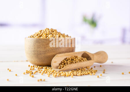 Lot of whole white mustard seeds with wooden bowl and wooden scoop with red flowers in a white kitchen