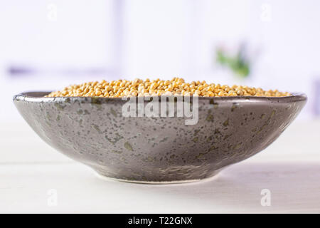 Lot of whole white mustard seeds on grey ceramic plate with red flowers in a white kitchen