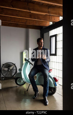 Man with motor scooter in a loft using cell phone Stock Photo