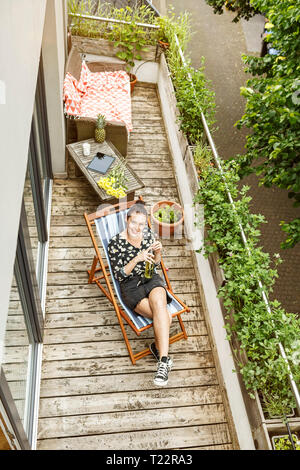 Young woman sitting in deck chair, relaxing on her balcony Stock Photo
