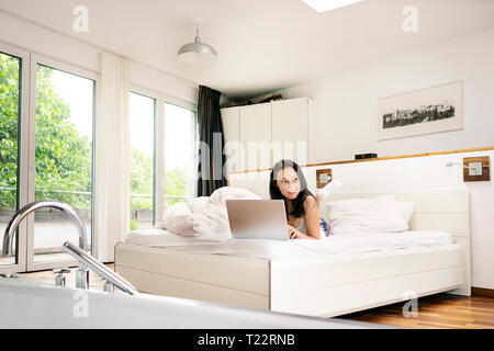 Young woman lying bed, using laptop in the morning Stock Photo