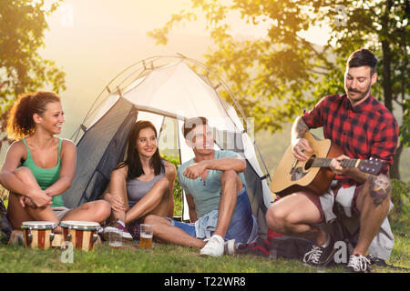 Young people enjoying in  music on camping trip, sitting next tent and singing with guitar Stock Photo