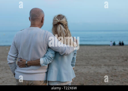 Spain, Barcelona, rear view of senior couple embracing on the beach at dusk Stock Photo