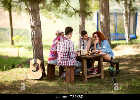 Two young female and male couples plays chess in summer camp in  woods Stock Photo