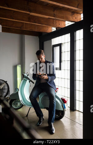 Man with motor scooter in a loft writing into notebook Stock Photo