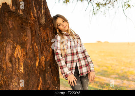 Portrait of blond girl leaning against tree trunk Stock Photo