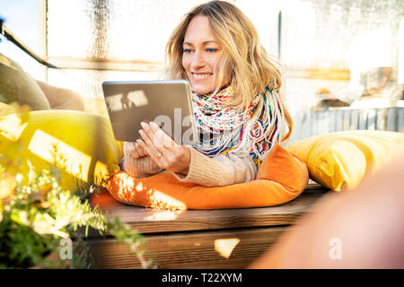 Portrait of smiling blond mature woman relaxing in winter garden using digital tablet Stock Photo