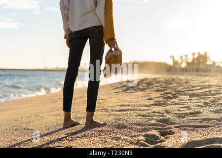 Barefoot woman on the beach, carrying her shoes Stock Photo