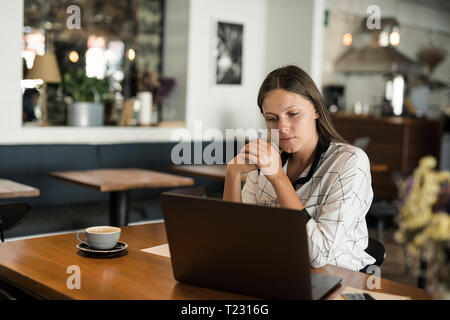 Young businesswoman in a cafe working with laptop on wooden table Stock Photo