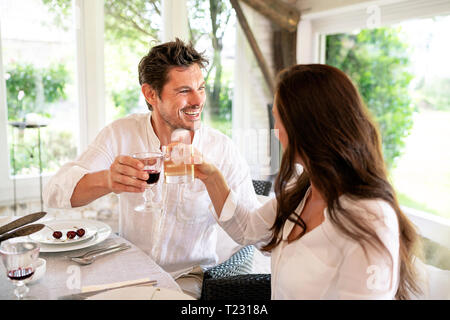 Happy couple clinking glasses at dining table Stock Photo