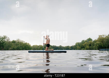 Senior man kneeling on SUP board Stock Photo