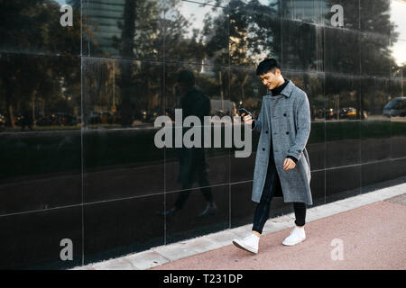 Spain, Barcelona, smiling young man looking at cell phone while walking in the city Stock Photo