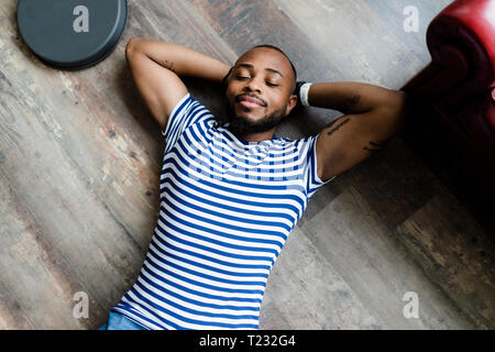Smiling young man lying on wooden floor with closed eyes Stock Photo