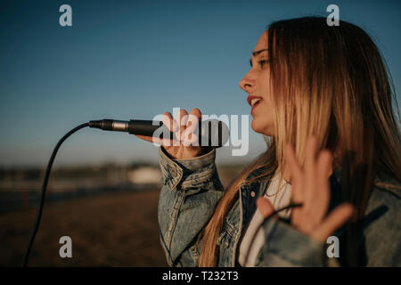 Young woman singing with a microphone outdoors Stock Photo