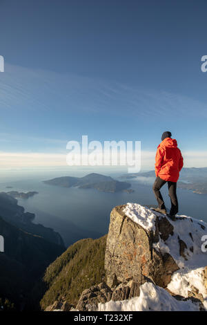 Male hiker standing on mountain peak overlooking ocean and islands Stock Photo